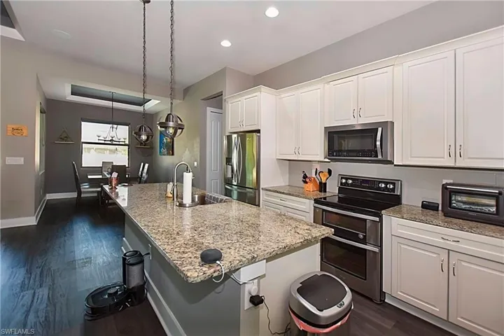 Kitchen with white cabinetry, stainless steel appliances, sink, dark hardwood / wood-style floors, and a kitchen island with sink