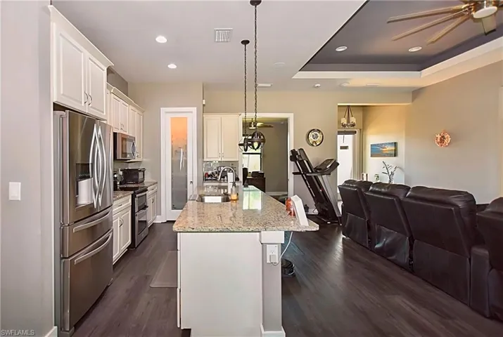 Kitchen featuring stainless steel appliances, sink, decorative light fixtures, an island with sink, and dark wood-type flooring