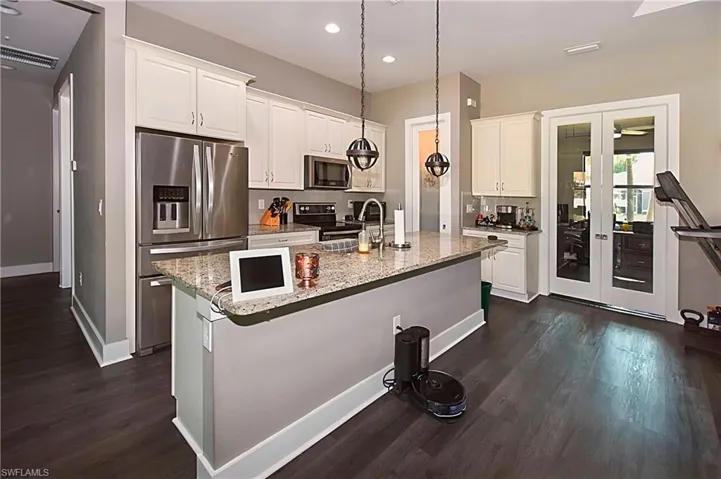 Kitchen with decorative light fixtures, white cabinetry, dark hardwood / wood-style flooring, an island with sink, and appliances with stainless steel finishes
