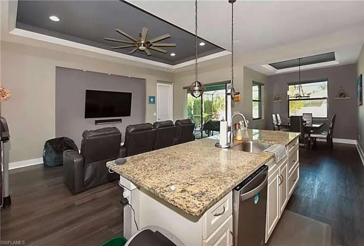 Kitchen with white cabinets, a center island with sink, a raised ceiling, and dark wood-type flooring