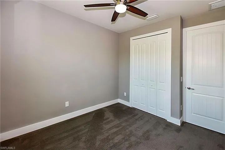 Unfurnished bedroom featuring a closet, ceiling fan, and dark carpet