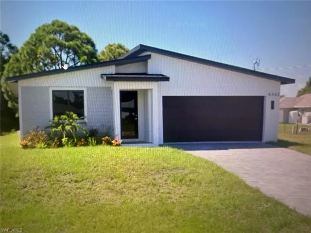 View of front of property with a front yard, decorative driveway, and a garage