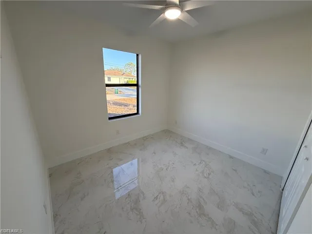 Unfurnished room featuring light marble finish floors and ceiling fan