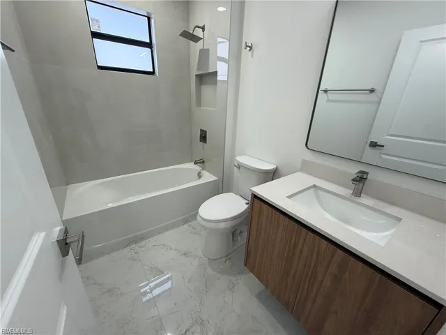 Bathroom with vanity, bathing tub / shower combination, and light marble finish floors