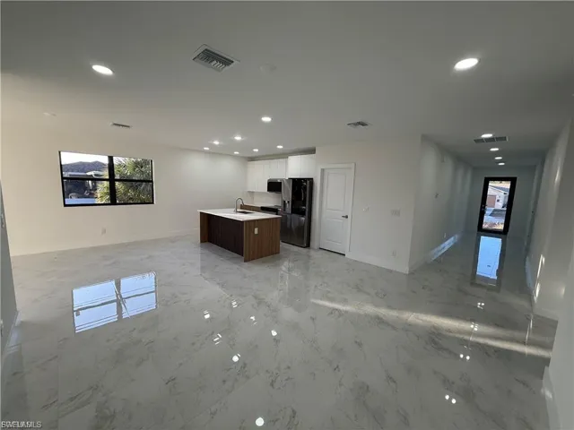 Kitchen with open floor plan, a center island with sink, stainless steel appliances, light countertops, and light marble finish floors