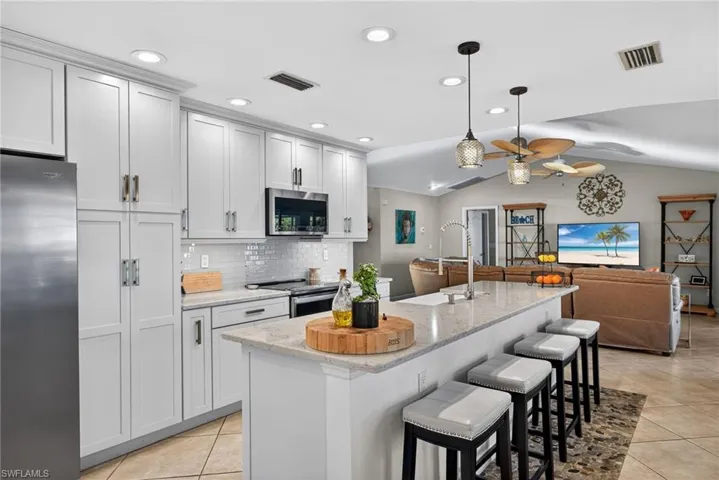 Kitchen featuring a kitchen breakfast bar, stainless steel appliances, light stone counters, open floor plan, and pendant lighting