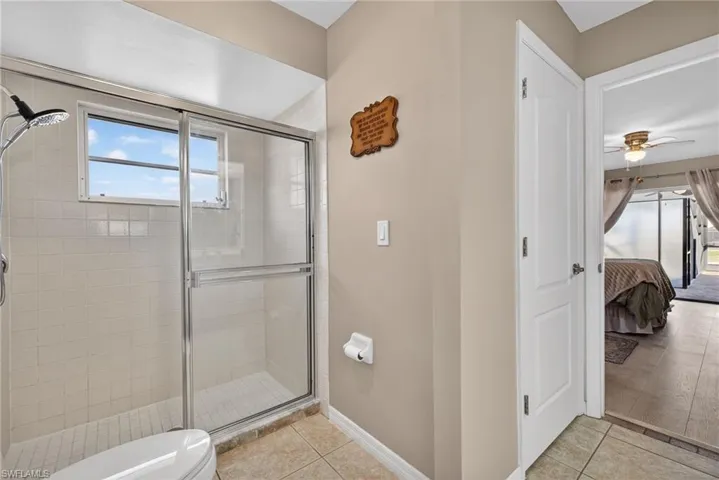 Ensuite bathroom with a stall shower, light tile patterned floors, and a ceiling fan