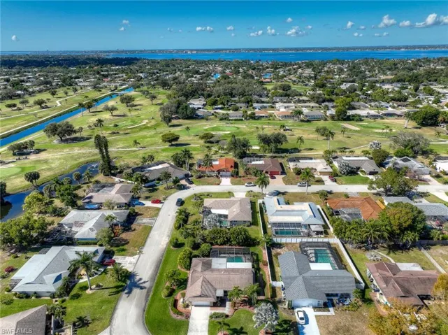 Aerial view of property and surrounding area featuring a golf course, a nearby body of water, and nearby suburban area