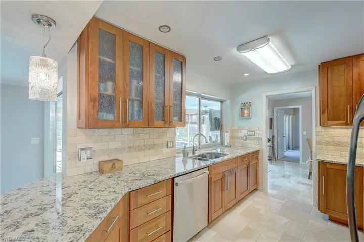 Kitchen with pendant lighting, light stone counters, glass insert cabinets, appliances with stainless steel finishes, and brown cabinets