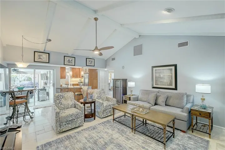 Living area with high vaulted ceiling, ceiling fan, and beam ceiling