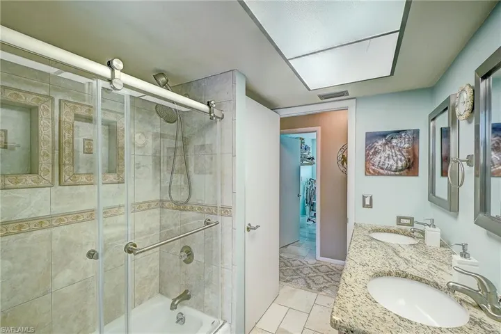 Full bath featuring double vanity, shower / bath combination with glass door, and light tile patterned flooring