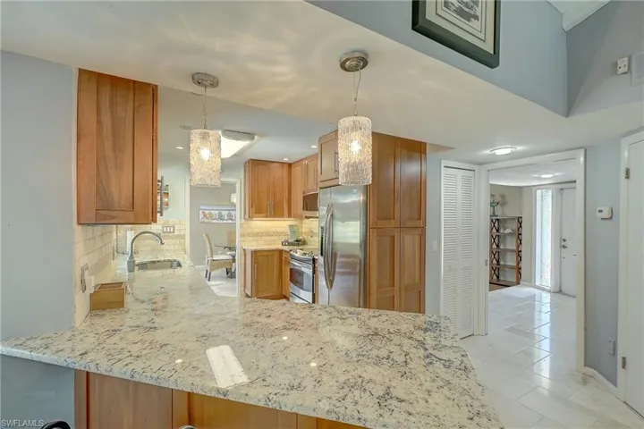 Kitchen with light stone counters, a peninsula, stainless steel appliances, and pendant lighting