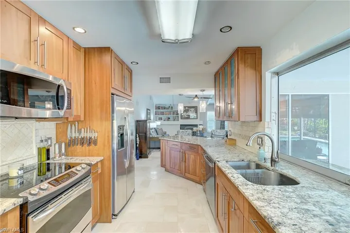 Kitchen featuring appliances with stainless steel finishes, light stone countertops, brown cabinetry, and recessed lighting