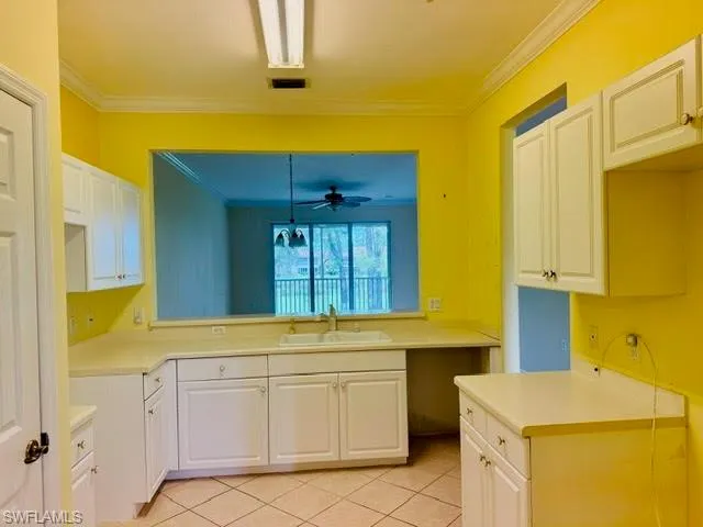 Kitchen with white cabinets, ornamental molding, light tile patterned floors, light countertops, and ceiling fan