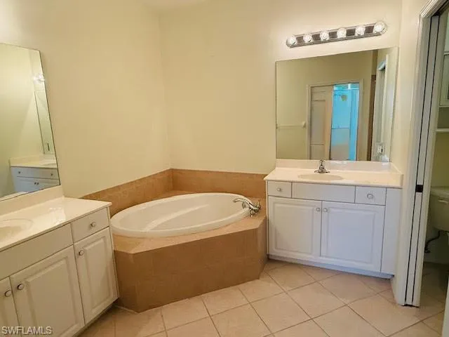 Full bath featuring light tile patterned flooring, a garden tub, and two vanities
