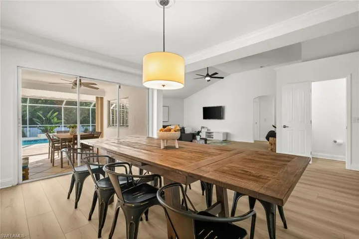 Dining room featuring crown molding, light wood-style flooring, a sunroom, a ceiling fan, and lofted ceiling