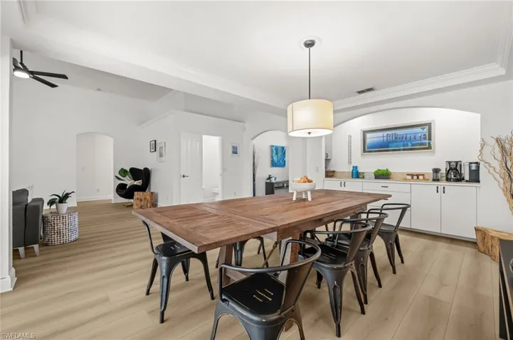 Dining space with arched walkways, light wood-style flooring, ornamental molding, and ceiling fan