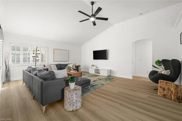 Living room featuring ornamental molding, lofted ceiling, a ceiling fan, arched walkways, and light wood-style floors