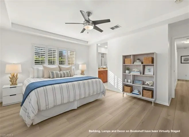 Bedroom featuring a raised ceiling, light wood finished floors, ensuite bathroom, and a ceiling fan