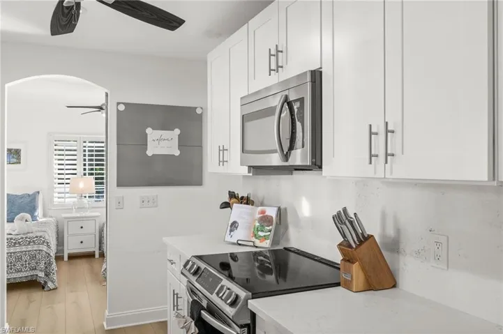 Kitchen with appliances with stainless steel finishes, white cabinetry, light wood-style flooring, and light stone counters