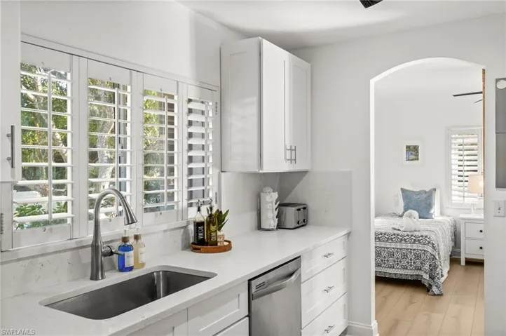 Kitchen featuring white cabinetry, stainless steel dishwasher, light stone countertops, light wood-style flooring, and arched walkways