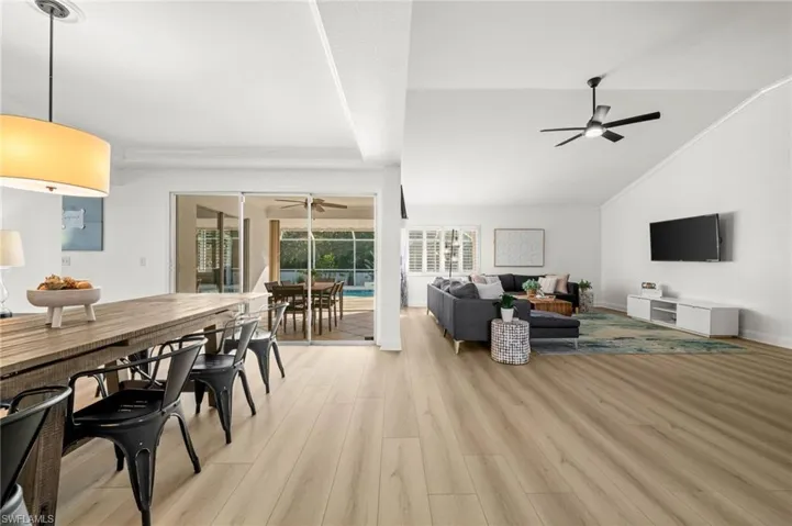 Living area with vaulted ceiling, light wood-style floors, a sunroom, ornamental molding, and ceiling fan