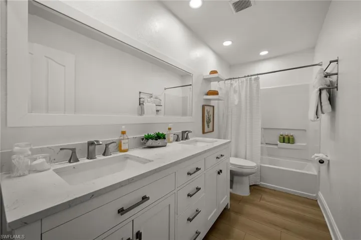 Bathroom with double vanity, shower / bath combination with curtain, light wood-style flooring, and recessed lighting