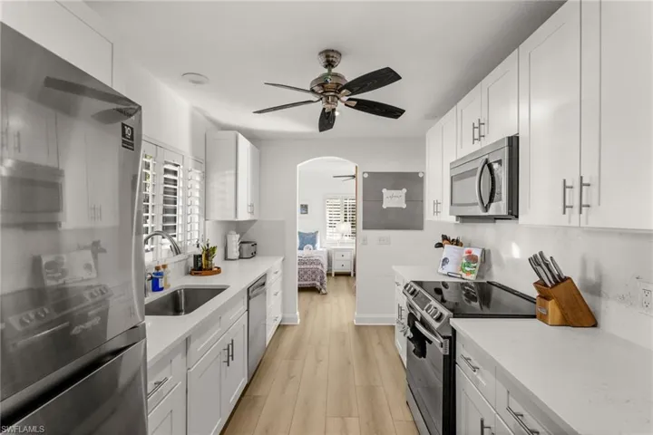 Kitchen featuring stainless steel appliances, ceiling fan, white cabinetry, and light stone countertops