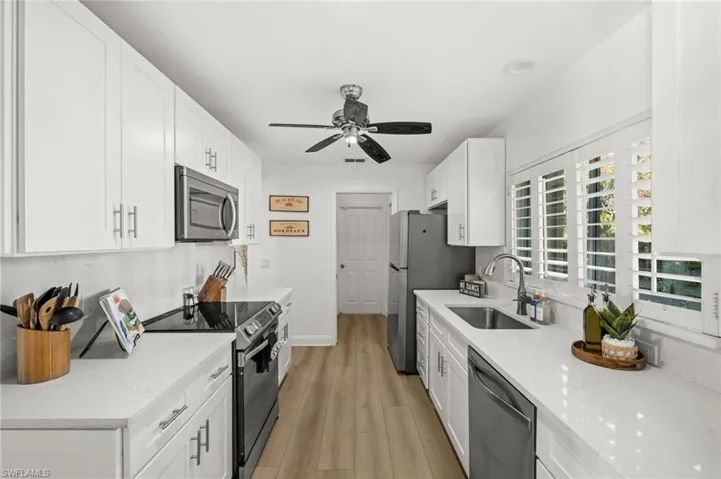 Kitchen featuring appliances with stainless steel finishes, white cabinetry, light stone countertops, and light wood-style floors