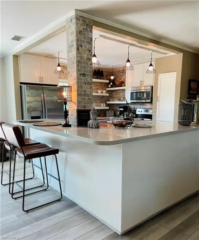 Kitchen with ornamental molding, appliances with stainless steel finishes, white cabinets, light wood-type flooring, and a breakfast bar