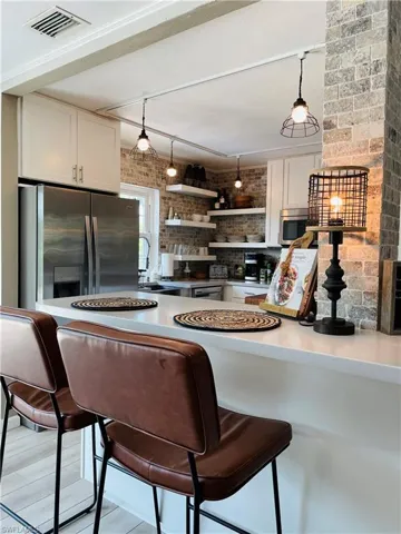Kitchen with appliances with stainless steel finishes, open shelves, pendant lighting, white cabinetry, and brick wall