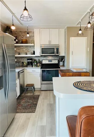 Kitchen featuring appliances with stainless steel finishes, white cabinetry, light wood-type flooring, hanging light fixtures, and ornamental molding