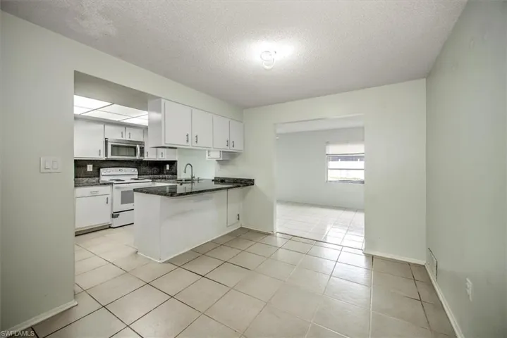 Kitchen featuring light tile patterned floors, kitchen peninsula, decorative backsplash, white electric range, and white cabinets