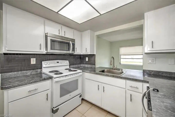 Kitchen with backsplash, sink, light tile patterned floors, white range with electric cooktop, and white cabinets