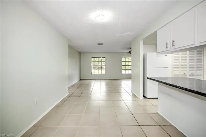 Kitchen with white fridge, light tile patterned floors, white cabinetry, ceiling fan, and a textured ceiling