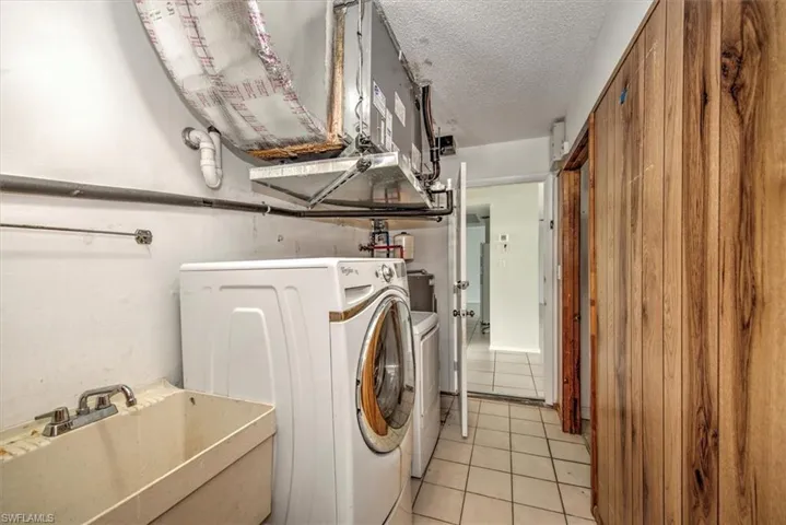 Washroom featuring washing machine and clothes dryer, light tile patterned floors, sink, and a textured ceiling