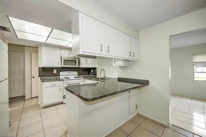 Kitchen with white cabinetry, sink, backsplash, kitchen peninsula, and electric range