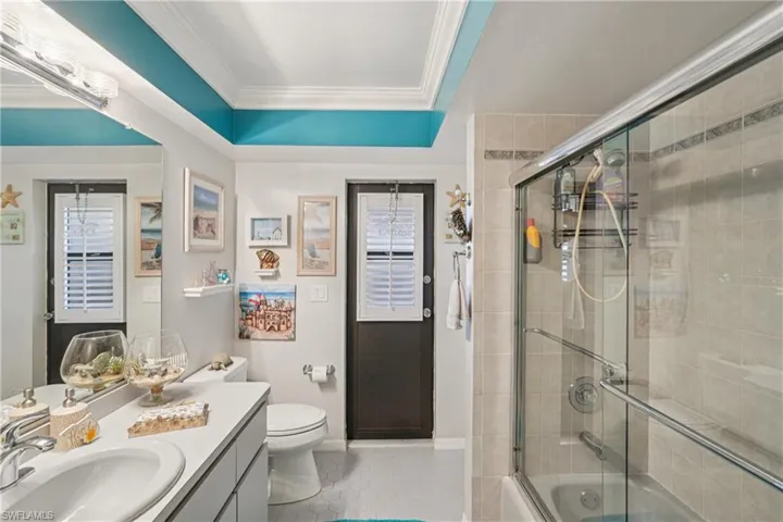 Full bath with shower / bath combination with glass door, ornamental molding, vanity, light tile patterned floors, and a raised ceiling