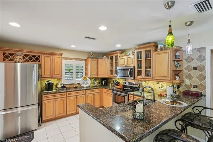 Kitchen with glass insert cabinets, appliances with stainless steel finishes, backsplash, dark stone countertops, and recessed lighting