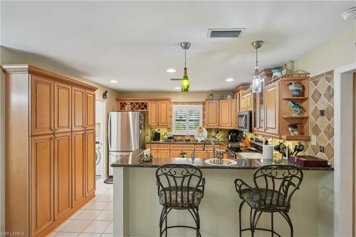 Kitchen with tasteful backsplash, brown cabinetry, light tile patterned flooring, stainless steel appliances, and hanging light fixtures