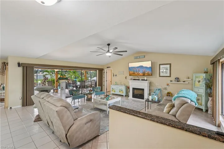 Living area featuring light tile patterned floors, vaulted ceiling, a glass covered fireplace, and ceiling fan