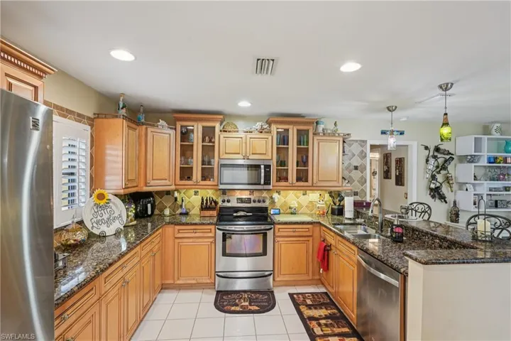Kitchen with a peninsula, stainless steel appliances, dark stone counters, decorative backsplash, and recessed lighting