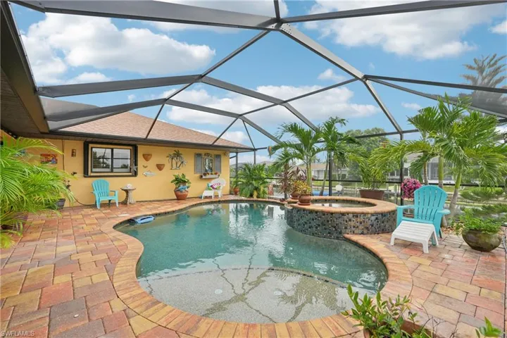 View of pool featuring a sunroom, a pool with connected hot tub, a patio area, and glass enclosure