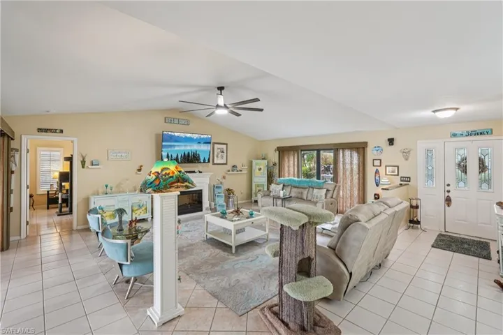 Living room with light tile patterned floors, lofted ceiling, a glass covered fireplace, and a ceiling fan