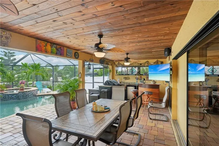 View of patio with glass enclosure, a sunroom, a pool with connected hot tub, exterior kitchen, and outdoor dining space