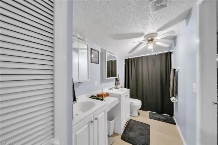 Guest house #2 Bathroom with a textured ceiling, two vanities, a shower with curtain, a ceiling fan, and a closet