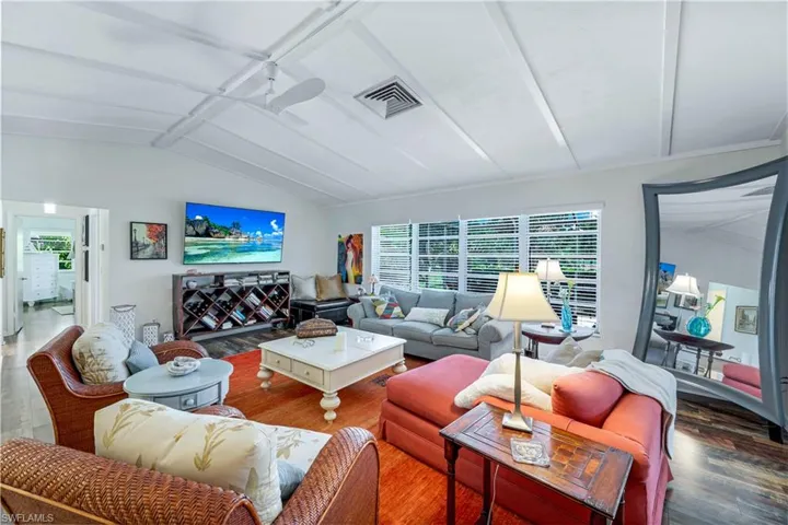 Living area with lofted ceiling with beams, visible vents, ceiling fan, large screen TV and wood finished floors