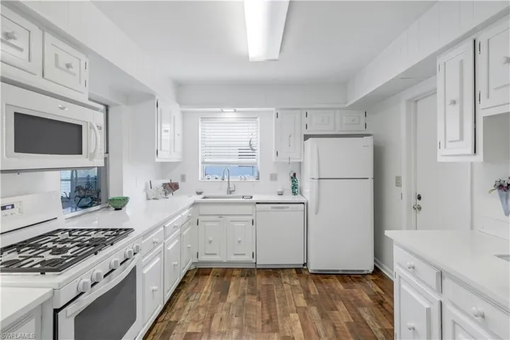 Kitchen with light countertops, a sink, a wealth of natural light, and white appliances.