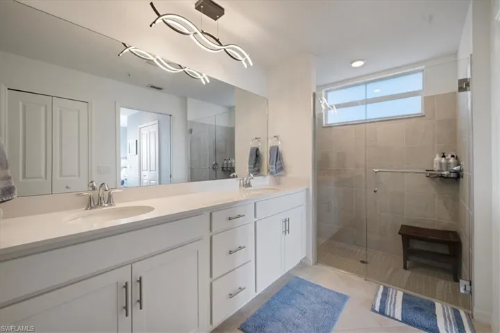 Full bath featuring a shower stall, double vanity, and light tile patterned floors