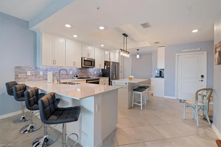Kitchen featuring a kitchen breakfast bar, a kitchen island, backsplash, white cabinetry, a tray ceiling and a coffee bar.